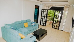 A living room with a light blue sofa, black coffee table, and a sliding glass door leading to a balcony. - Igitego Hotels (Kigali)