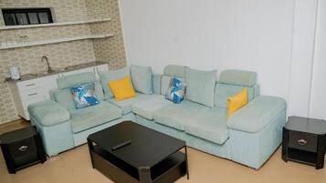 Un salón con un sofá azul claro, dos almohadones amarillos, una mesita de centro negra y una mesita auxiliar pequeña negra.