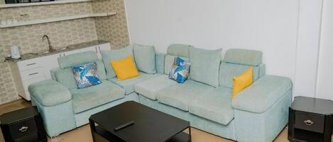 A living room with a light blue sofa, two yellow pillows, a black coffee table, and a small black side table.