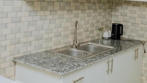 A kitchen with a granite countertop, white cabinets, a stainless steel sink, and a black coffee maker. - Igitego Hotels (Kigali)