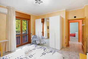 Ein Schlafzimmer mit Bett, Schreibtisch, Stuhl, Kleiderschrank und einem Balkon.