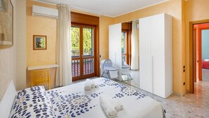 A bedroom with a bed, a desk, a chair, a wardrobe, and a balcony.