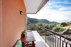 Ein Balkon mit Holztisch und -stühlen, einem Topfpflanzen und Blick auf eine hügelige Landschaft.