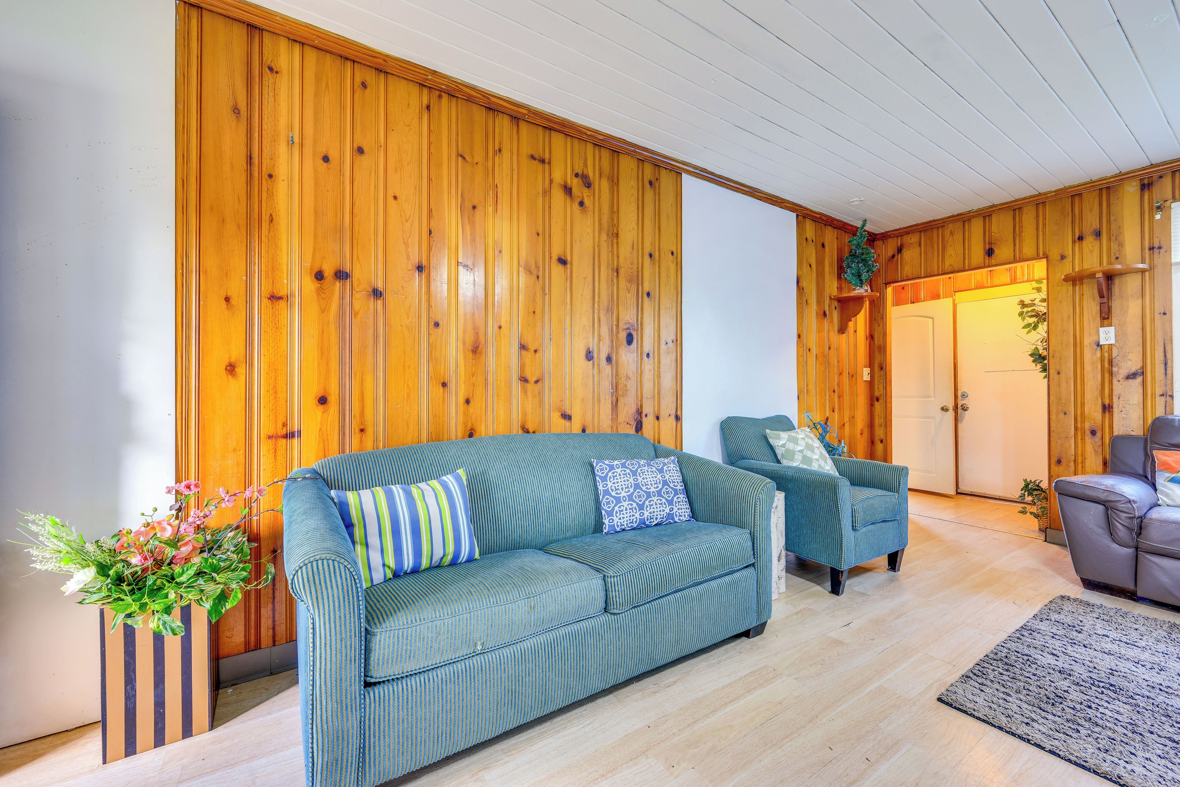 A room with a wooden paneled wall, a green sofa, a striped armchair, and a grey sofa.