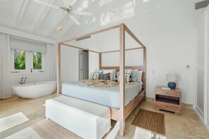 Een slaapkamer met een hemelbed, een badkuip, een nachtkastje met een lamp en een groot raam met gordijnen.