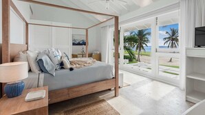 A four-poster bed with a view of the beach, a ceiling fan, and a TV on a stand.