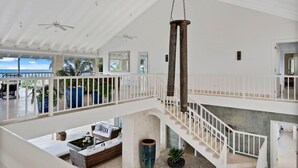 A spacious indoor area with a high ceiling, a central column, a staircase, and a view of the ocean.