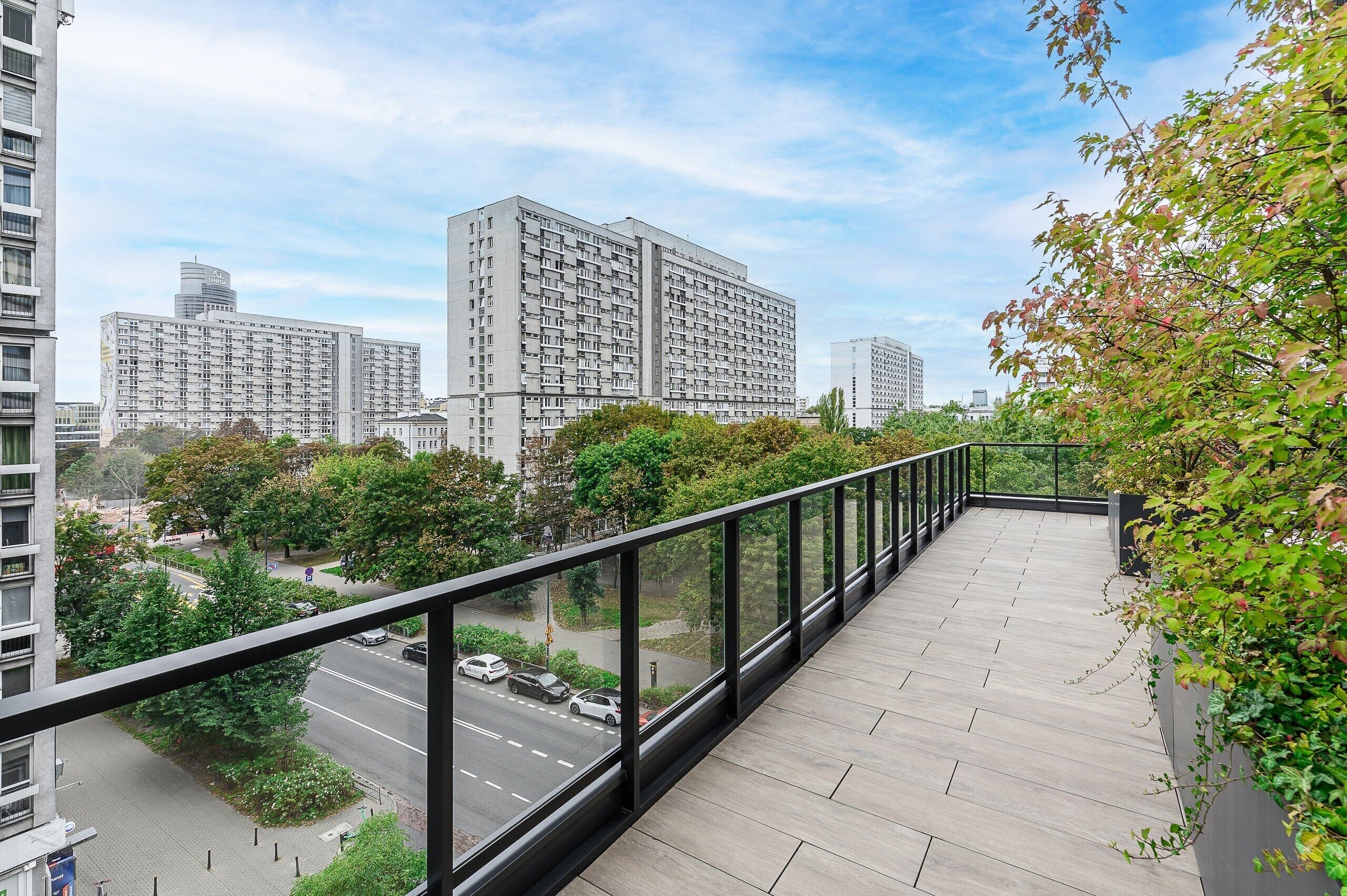 A balcony with a view of a cityscape, including tall buildings and a road with cars.