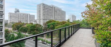 A balcony with a view of a cityscape, including tall buildings and a road with cars.