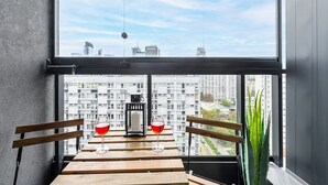 A balcony with a table, two glasses of red wine, a lantern, and a potted plant. - Lumina 15th Floor Apartment in Warsaw  (Warsaw)