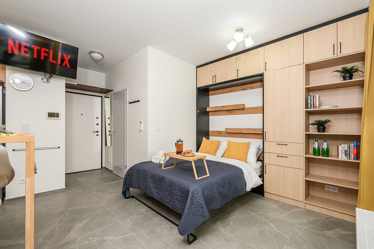 Une chambre à coucher de taille réduite, comprenant un lit, une table de chevet et une étagère avec des livres et une plante.