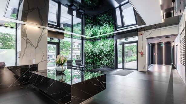A modern lobby with a marble reception desk, large windows, and a green wall. - Lumina 15th Floor Apartment in Warsaw  (Warsaw)