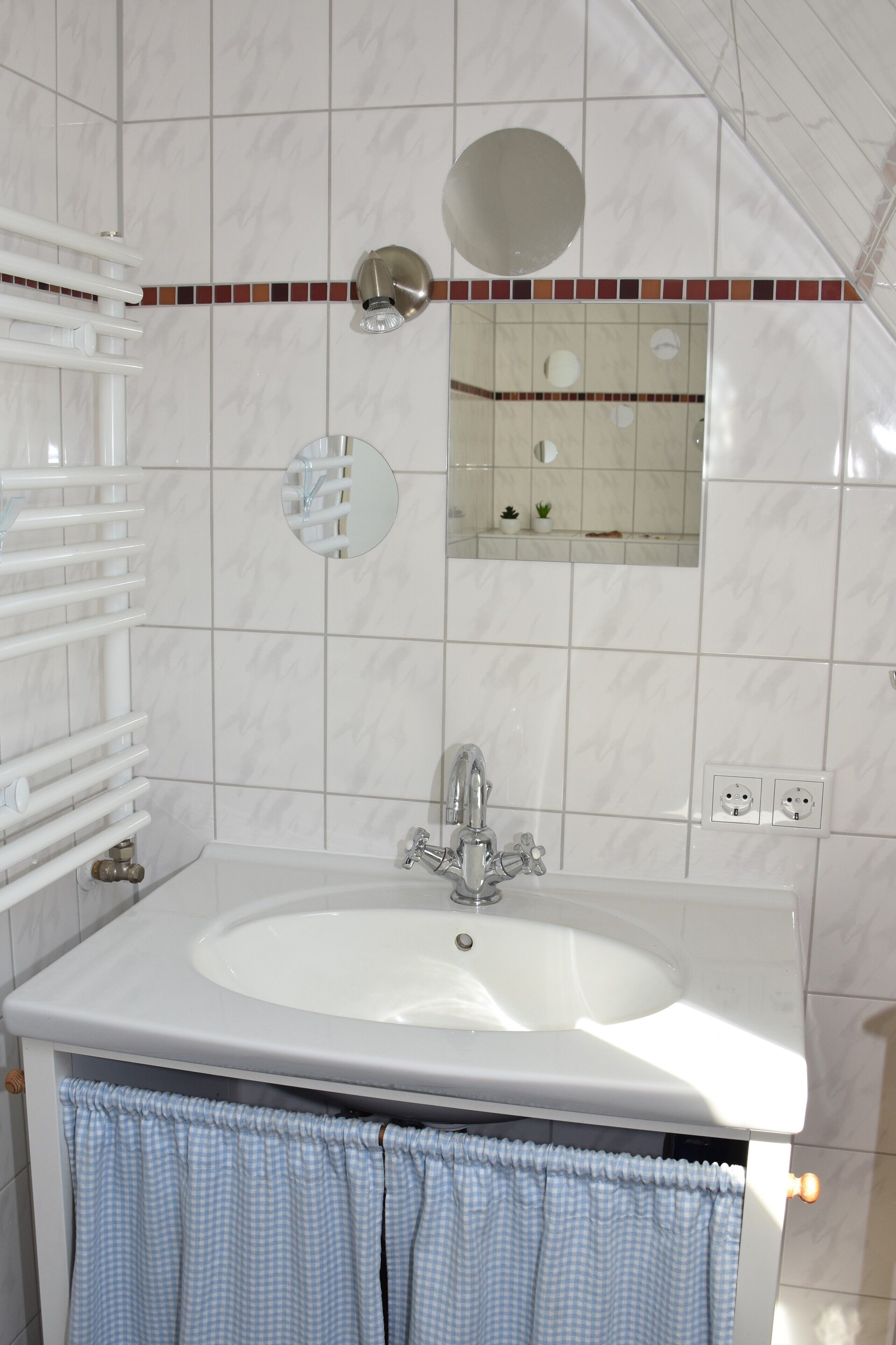 A bathroom with a white sink, a mirror, a towel rack, and a tiled wall.