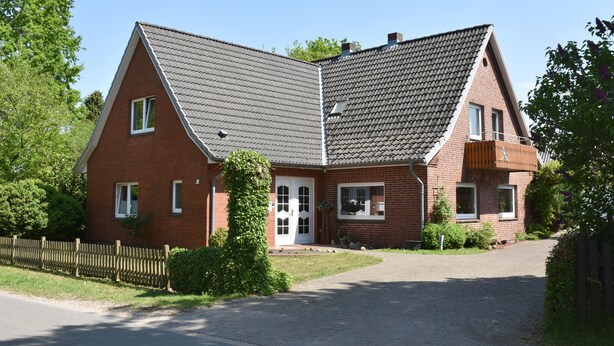 A two-story brick house with a sloped roof, a front door, and a driveway.