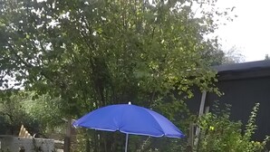 An outdoor patio with a table and chairs, a blue umbrella, and a stone wall.