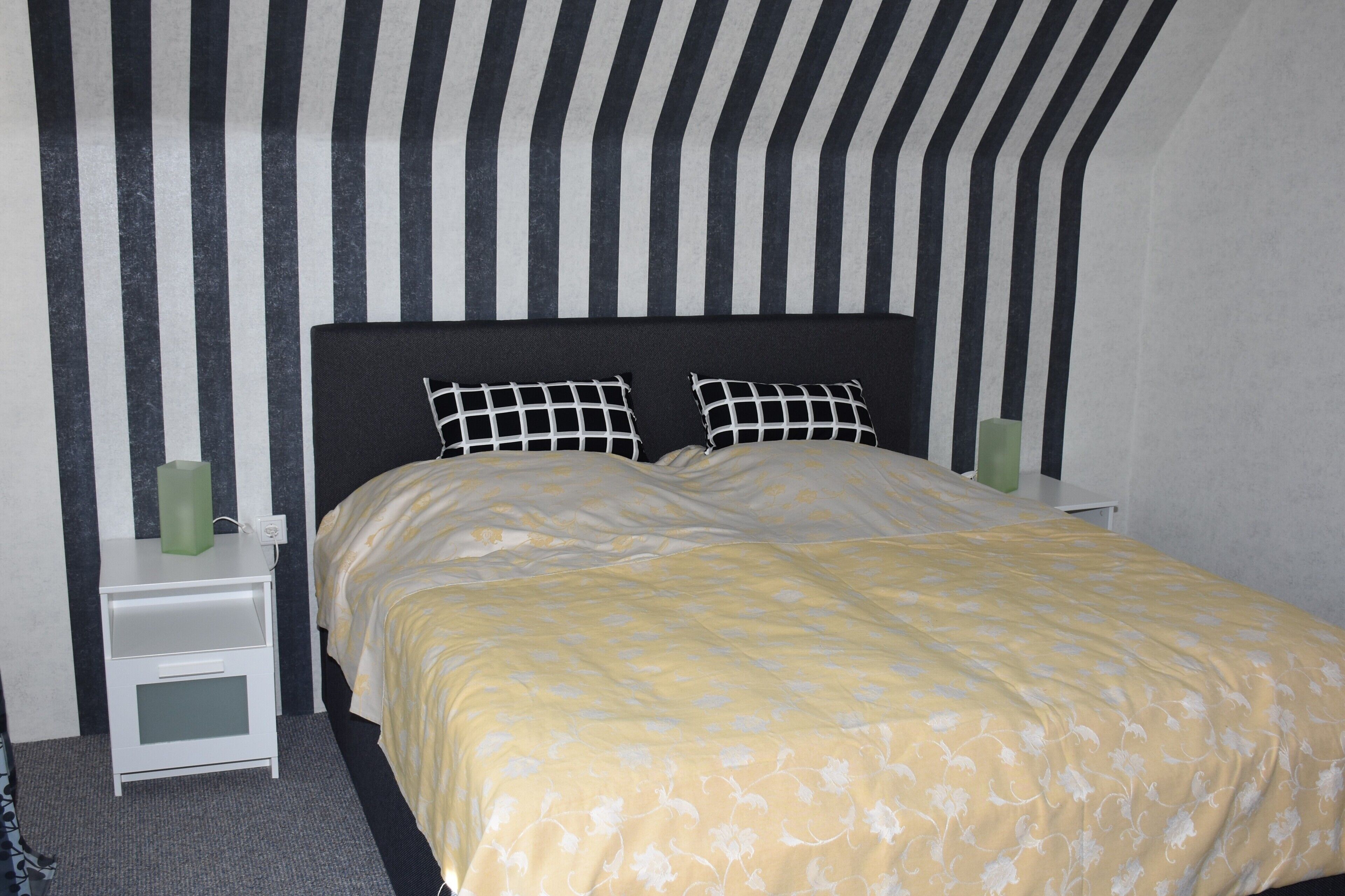 A bed with a floral-patterned bedspread, a black and white striped headboard, and two bedside tables with green vases.