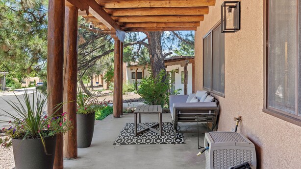 A covered patio area with a wooden pergola, a seating area with a table and chairs, and potted plants.