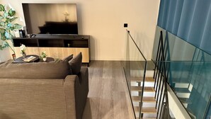 A modern living room with a sofa, a TV, a wooden cabinet, and a staircase with glass railings. - Madrid Dream House (Madrid)