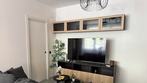 A modern living room with a large flat-screen TV, a dark grey sofa, a small round coffee table, and a decorative plant. - Madrid Dream House (Madrid)