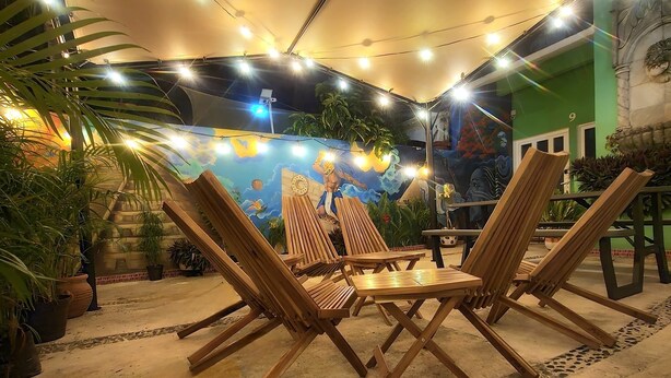 An outdoor seating area with wooden chairs and tables under a canopy, surrounded by potted plants and a mural. - Villa Leo Room with bunk bed ideal for families, in the heart of Cancun (Cancun)