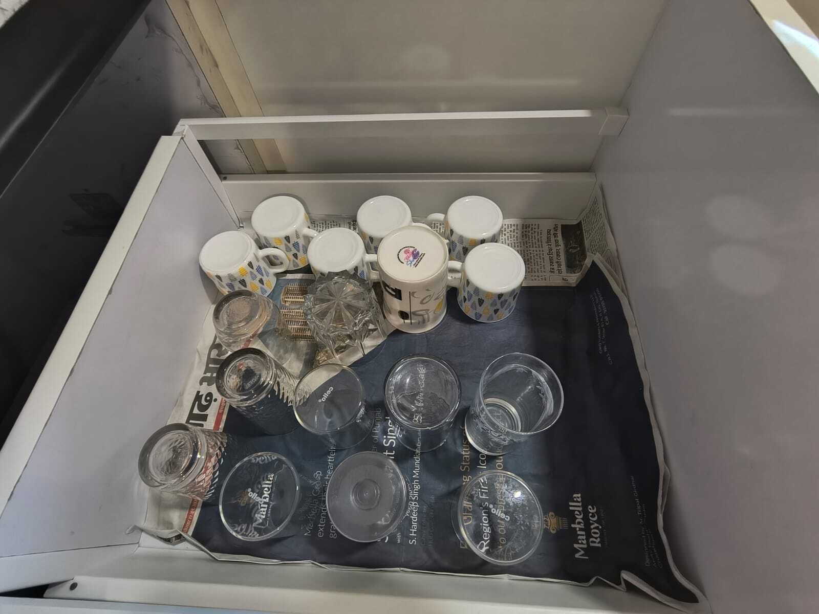 A drawer containing various items including mugs, glasses, and CDs.
