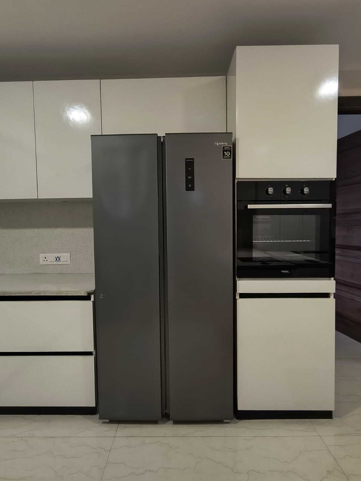 A modern kitchen with two stainless steel refrigerators, a built-in oven, and white cabinetry.