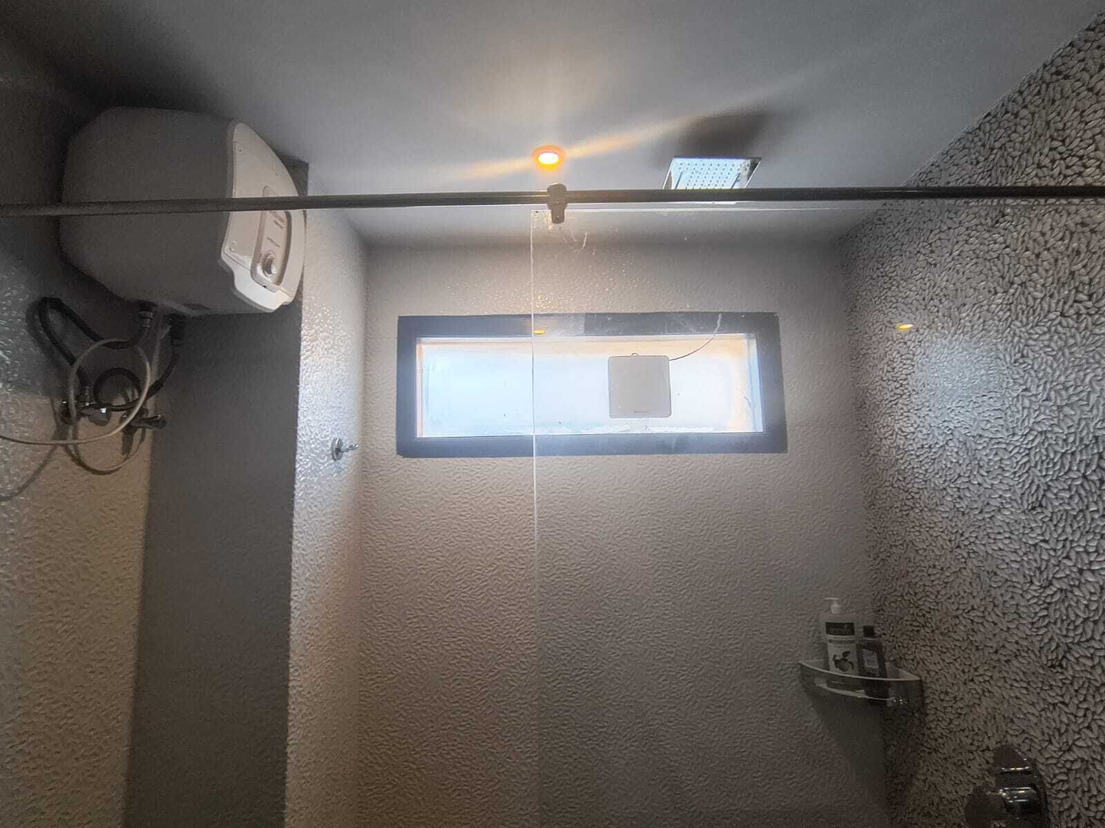 A small, enclosed shower area with a window, a towel rack, and a wall-mounted air conditioner.