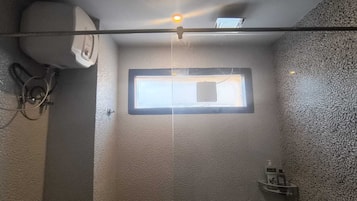 A small, enclosed shower area with a window, a towel rack, and a wall-mounted air conditioner.
