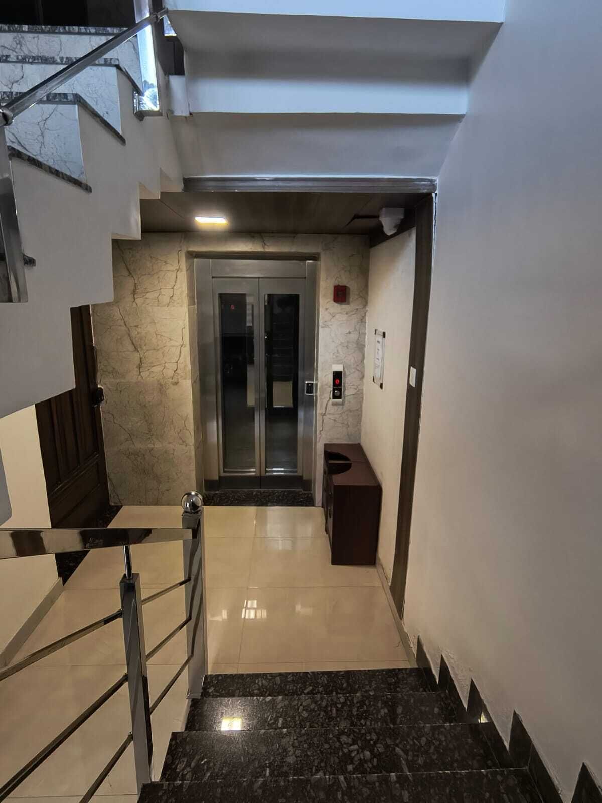 Un ascenseur moderne doté d’une porte en verre, d’un mur en marbre et d’une main courante en métal.