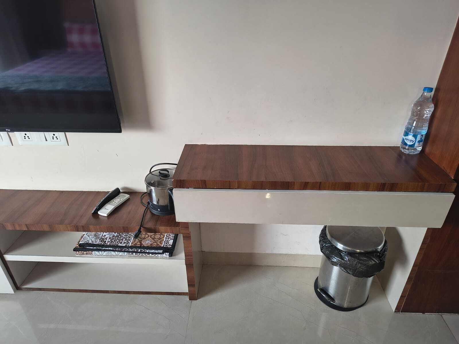 A small, modern room with a wooden desk, a trash bin, a water bottle, and a television.