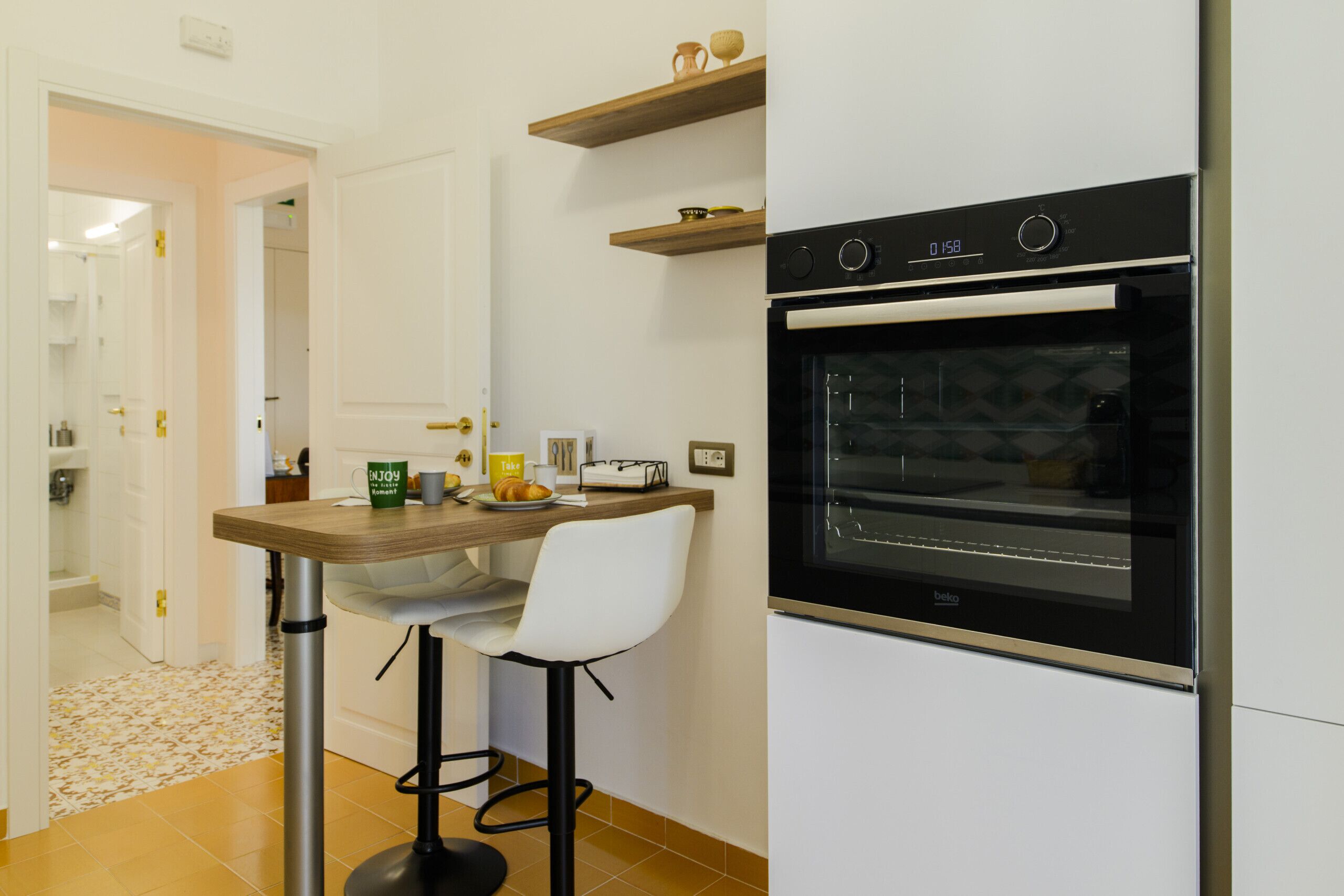 A kitchen with a modern oven, a wooden table with a chair, and a door leading to another room.