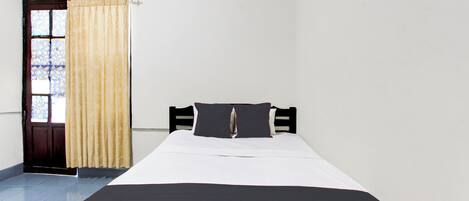 A single bed with a black and white bedspread, a wooden headboard, and a window with a curtain.
