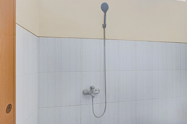 A shower with a handheld showerhead and a wall-mounted faucet.