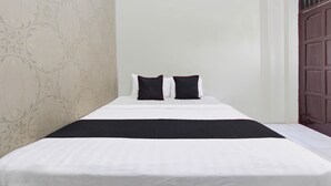 A neatly made bed with white bedding and two black pillows, a dark throw blanket, and a floral wallpaper pattern on the left wall. - Hotel O Near Tugu Yogyakarta 2 formerly Monjali Inn (Sinduadi)