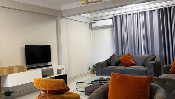 Uma sala de estar moderna com televisão de tela plana, ventilador de teto, sofá cinza e poltrona amarela.