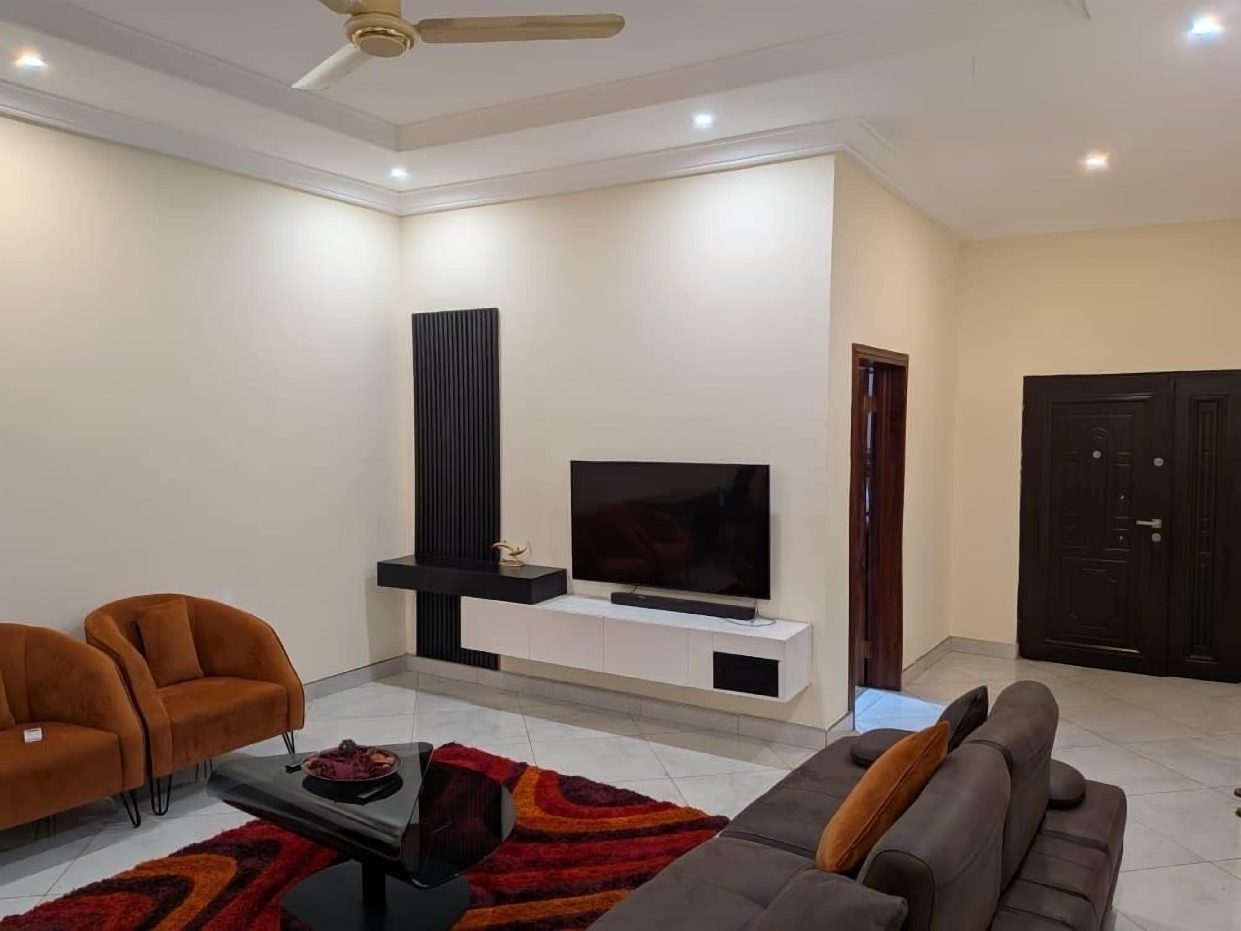 A modern living room with a flat-screen TV, a black entertainment unit, a brown sofa, a grey sofa, and a red and black rug.