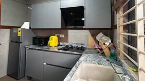 Uma cozinha moderna com armários cinzas, micro-ondas embutido, chaleira amarela e pia com bancada de mármore.