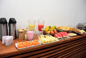 Una mesa de buffet con diversas frutas, jugos y alimentos para el desayuno.