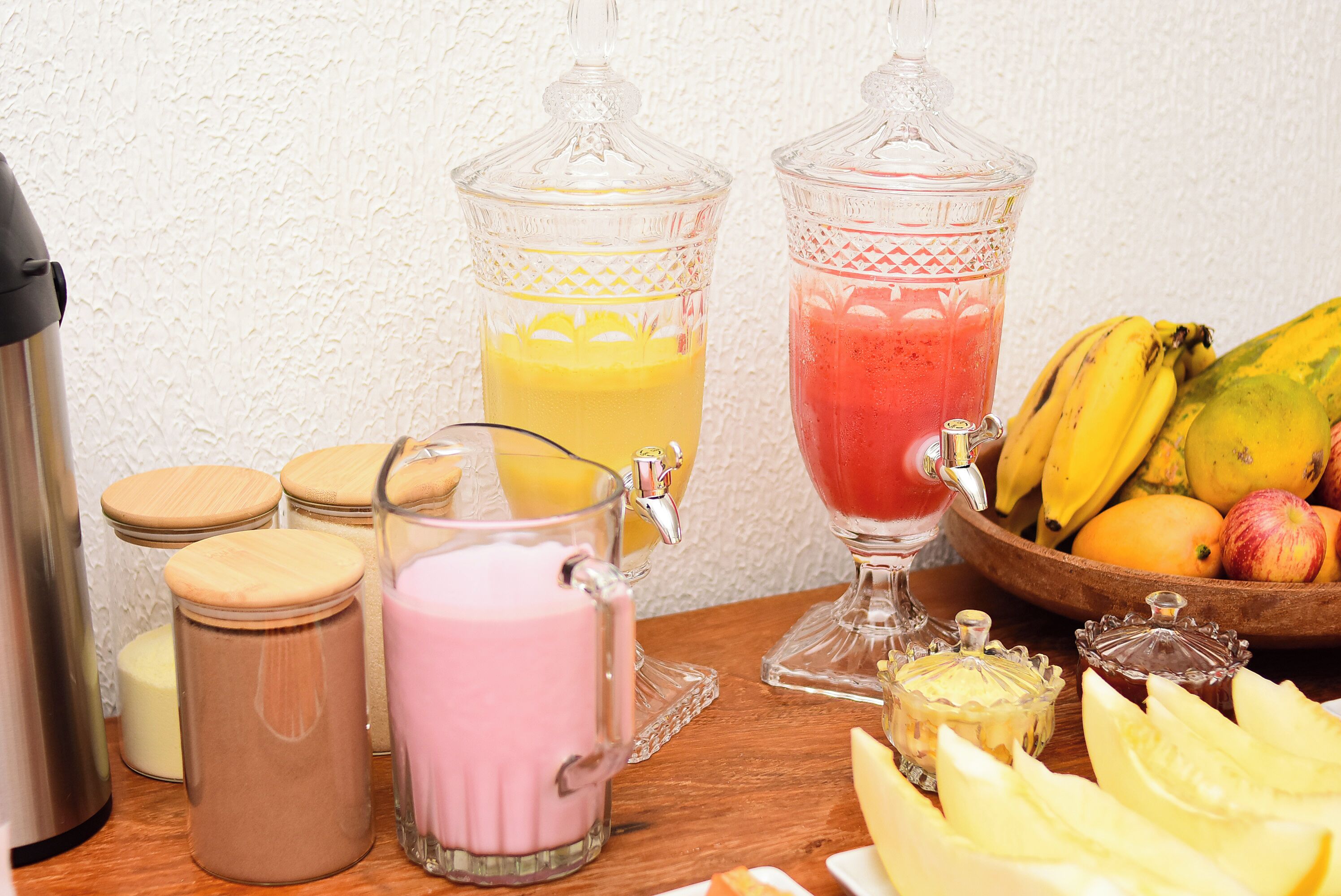 Une table de petit-déjeuner avec deux extracteurs de jus de fruits, un thermos et un saladier rempli de fruits.