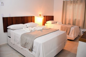 Habitación de hotel con dos camas, cabecero de madera, mesita de noche con lámpara y ventana con cortinas.
