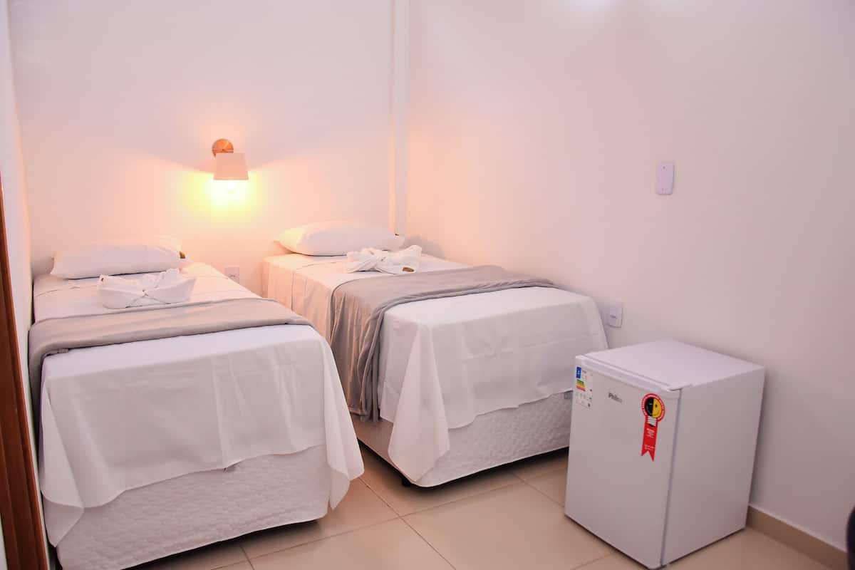 Une chambre d’hôtel avec deux lits simples, un petit réfrigérateur et un luminaire fixé au mur.