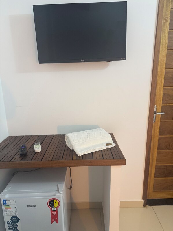 A small room with a wooden desk, a white towel, a white appliance, and a flat-screen TV mounted on the wall. - HOTEL IPE (Barreirinhas)