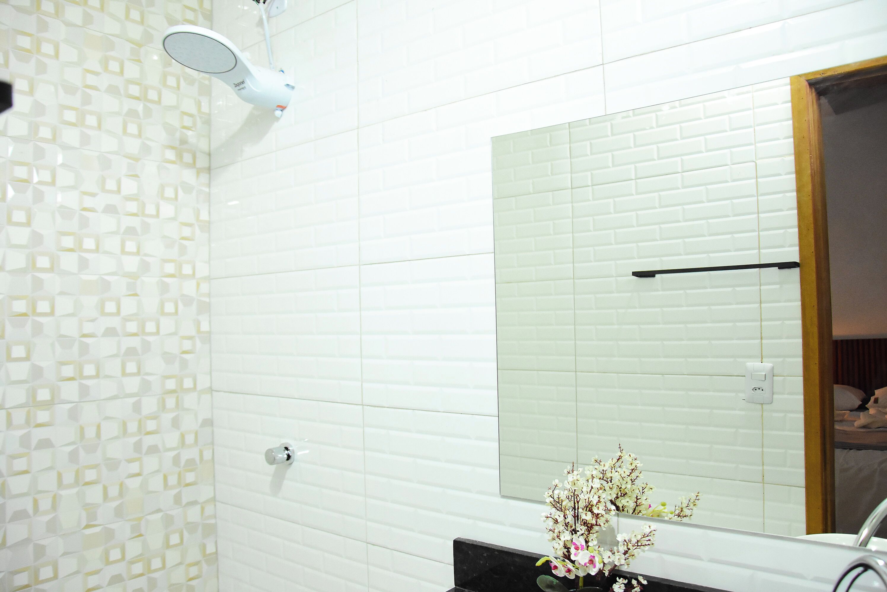 A bathroom with a white tiled wall, a mirror, a black countertop, and a flower arrangement.