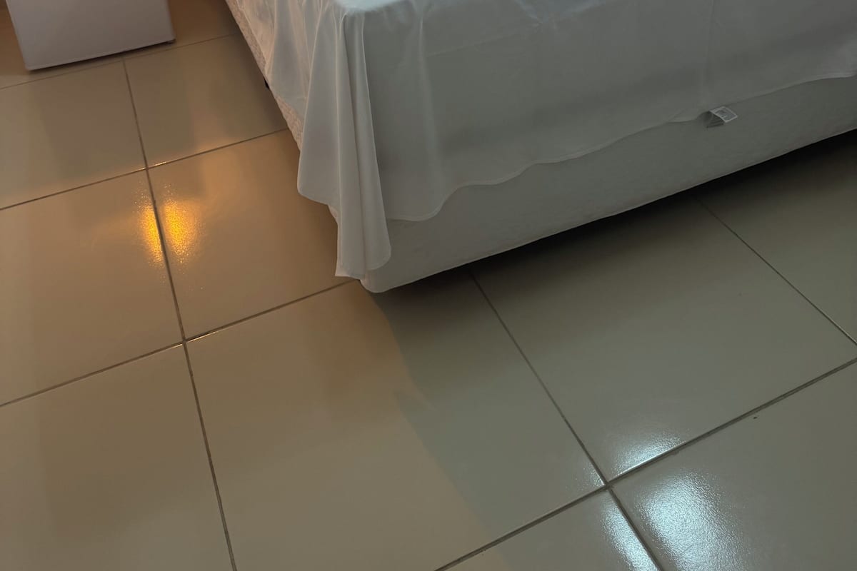 Une chambre d’hôtel propre et bien éclairée, avec un lit soigneusement fait, une petite table de chevet avec une lampe et un mini-bar.