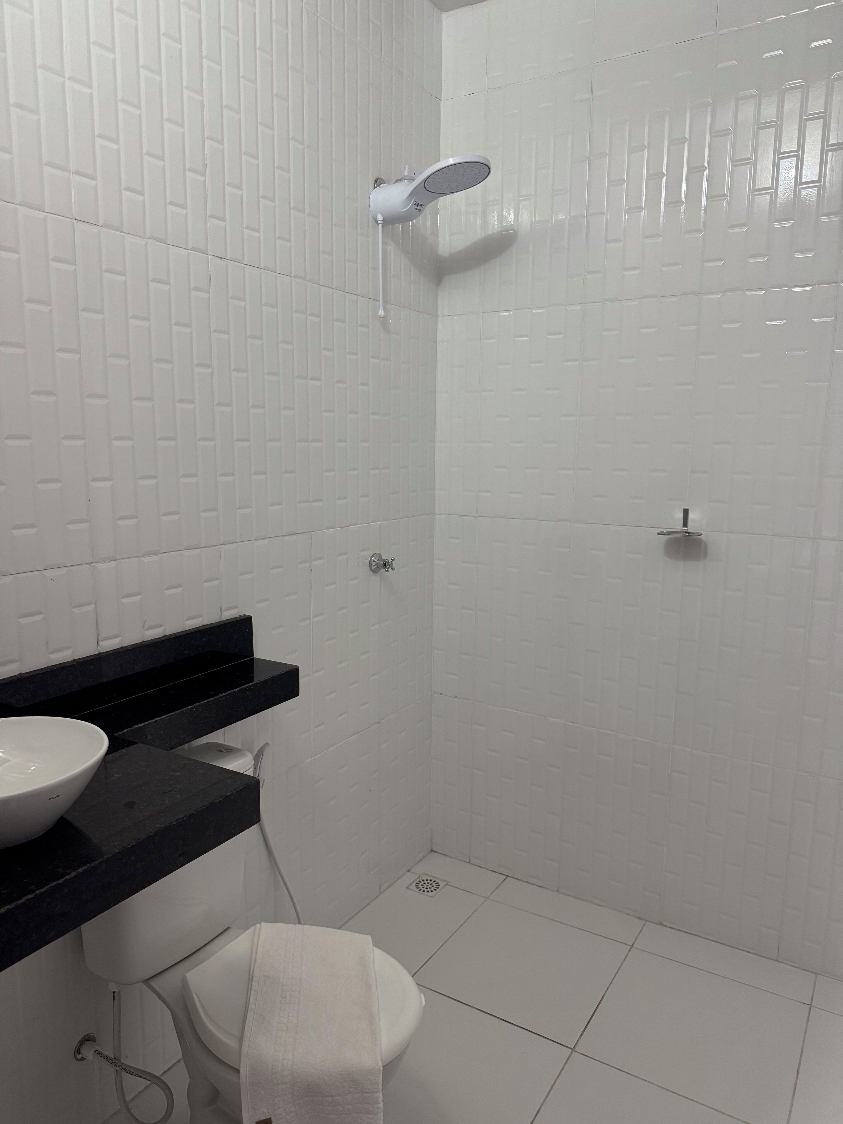 A bathroom with white tiled walls, a black countertop, a white sink, a toilet, and a shower with a handheld showerhead.