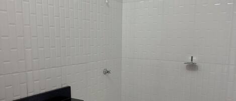 A bathroom with white tiled walls, a black countertop, a white sink, a toilet, and a shower with a handheld showerhead.