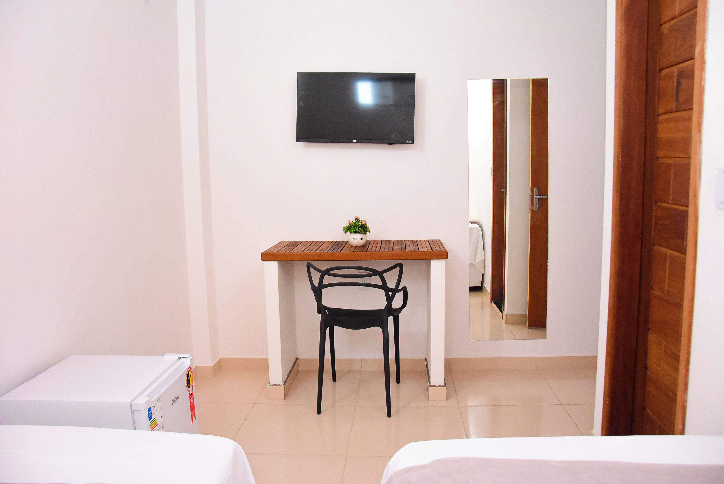 Ein kleines Zimmer mit einem Bett, einem Schreibtisch, einem Sessel, einem Fernseher und einem Spiegel.