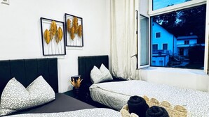 A bedroom with two beds, a window with a view of a building, and wall art. - Compact Studio Apartment with Essentials, Ideal for 2 Guests (Wien)