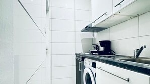 A compact kitchen with a washing machine, a coffee maker, and a sink. - Compact Studio Apartment with Essentials, Ideal for 2 Guests (Wien)
