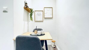 A small dining area with a table, chairs, a shelf with a plant, and two framed artworks on the wall. - Compact Studio Apartment with Essentials, Ideal for 2 Guests (Wien)